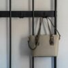 Stylish grey leather purse with gold details hanging on a modern black hook against a minimalist backdrop.