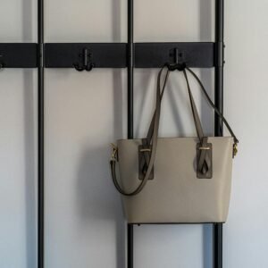 Stylish grey leather purse with gold details hanging on a modern black hook against a minimalist backdrop.